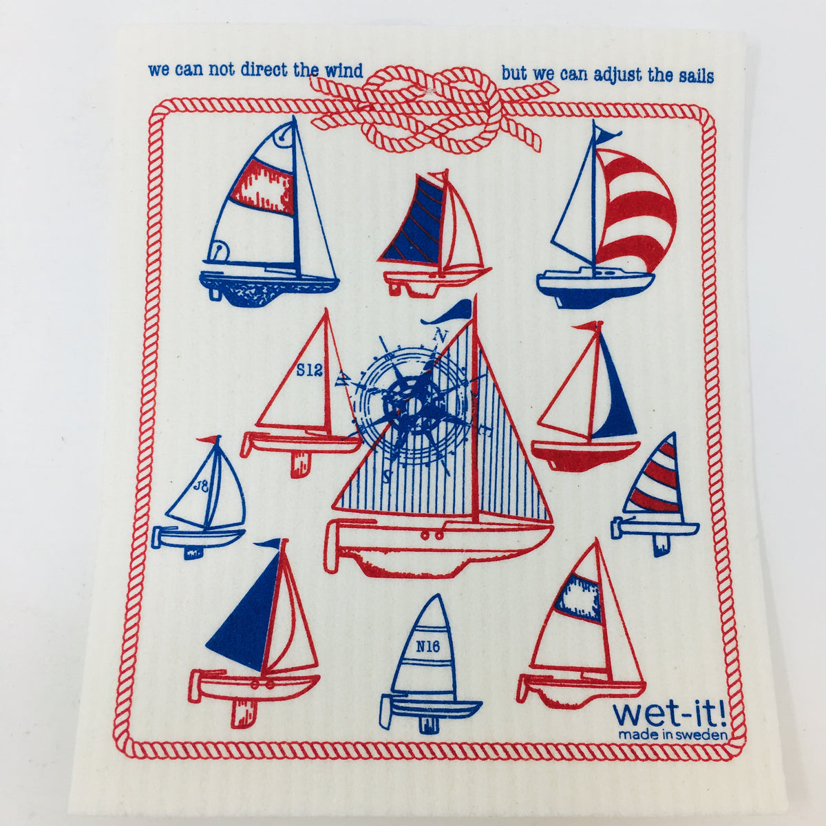 ivory colored rectangle shaped scrubbing pad with multiple sailboat drawings in reds and blues inside a nautical rope themed red border and the message &quot;we can not direct the wind but we can adjust the sails&quot; screen printed on it