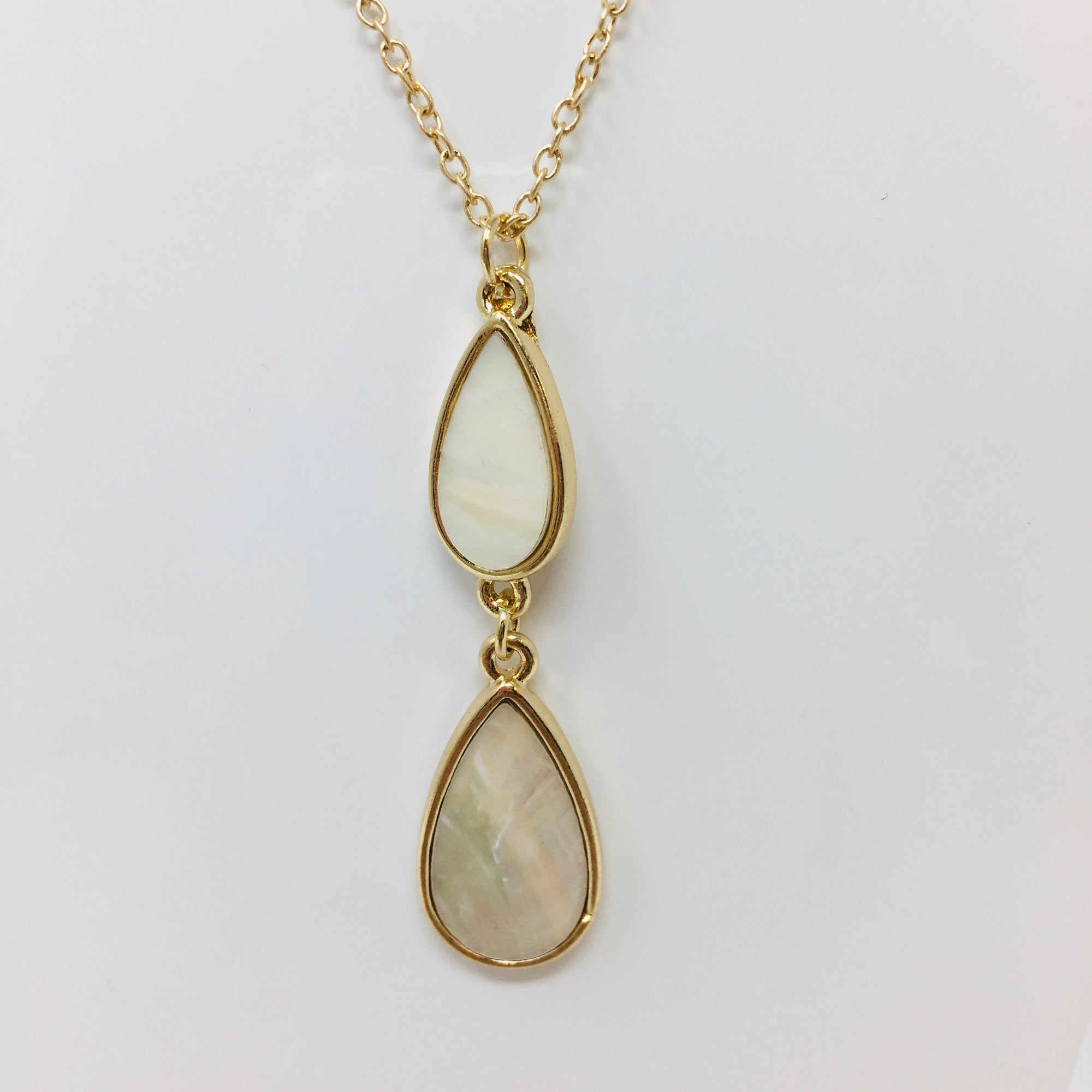 gold tone chain necklace with double teardrop pendant with mother of pearl inserts in the teardrops shown on a white bust form on white background