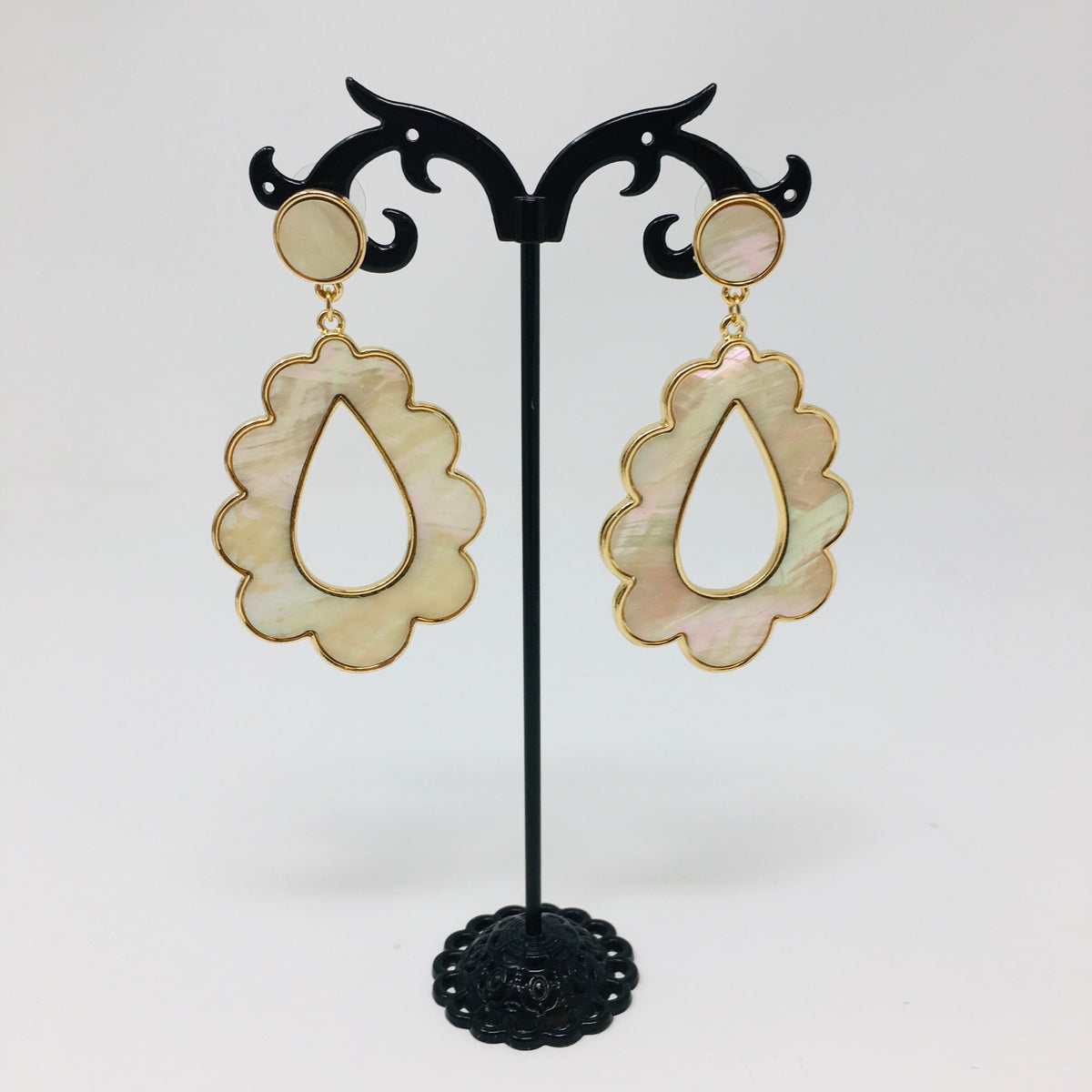 Scalloped teardrop shaped gold tone earrings with mother of pearl inserts shown hanging from a black earring stand on a white background