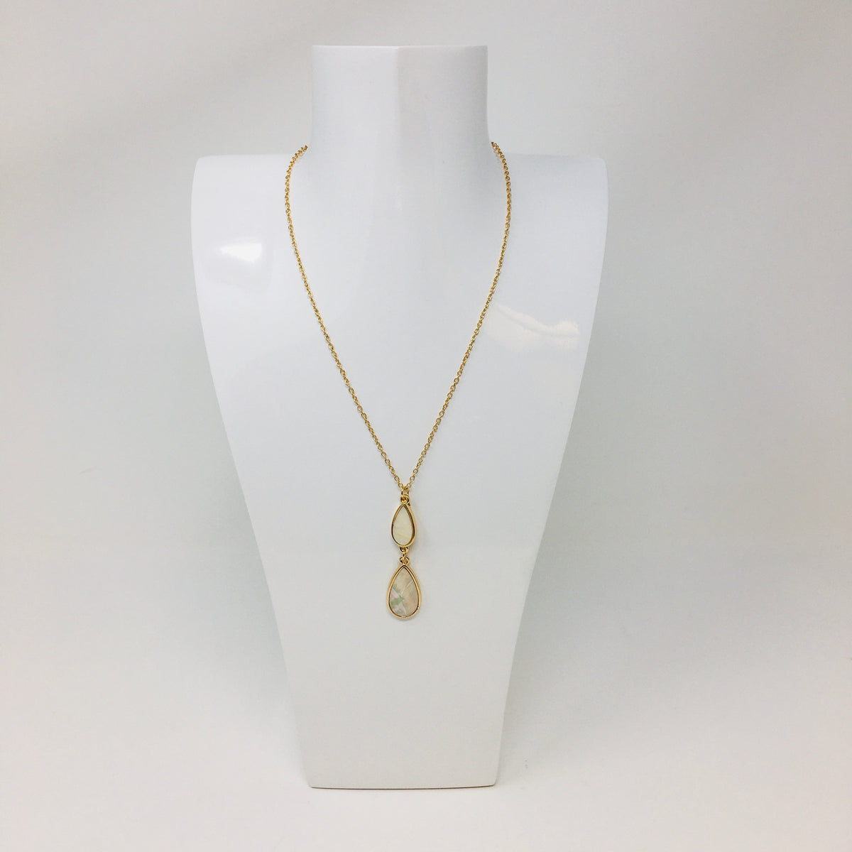 gold tone chain necklace with double teardrop pendant with mother of pearl inserts in the teardrops shown on a white bust form on white background