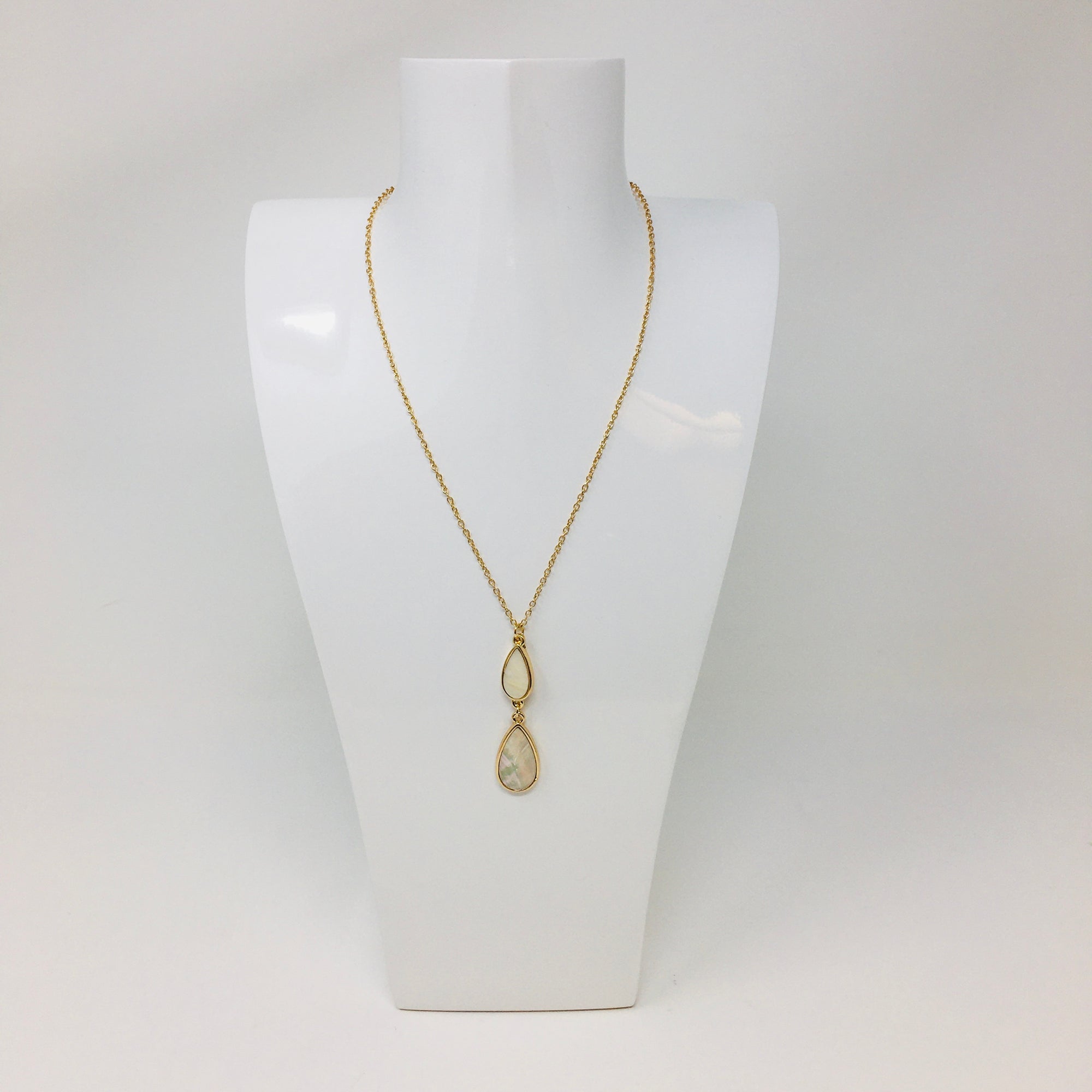 gold tone chain necklace with double teardrop pendant with mother of pearl inserts in the teardrops shown on a white bust form on white background