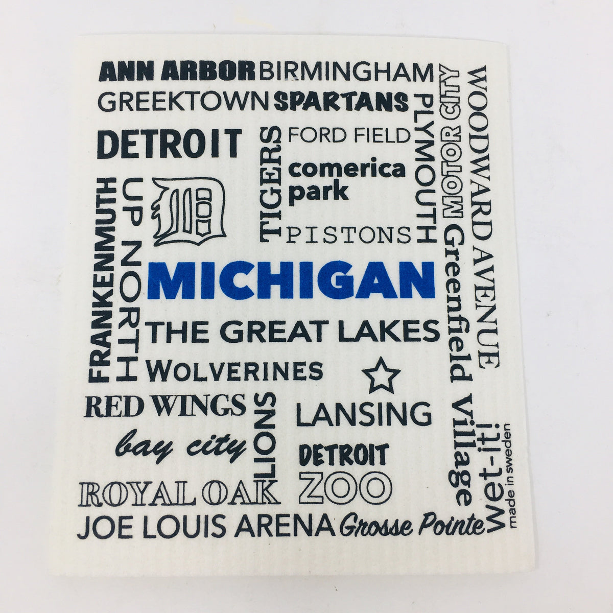 ivory colored rectangle shaped scrubbing pad with Michigan city names and attractions such as &quot;Frankenmuth, Ann Arbor, Joe Louis Arena, The Great Lakes, Motor City&quot; printed all over it in black and &quot;Michigan&quot; printed in blue on it