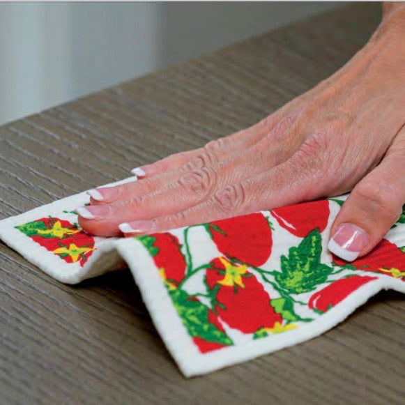 A lightly dampened wet-it towel shown in use with a hand on it wiping it across a wooden surface cleaning the surface